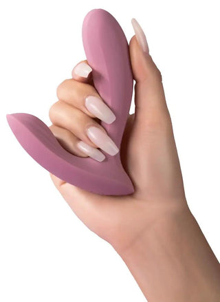 Handen håller en Svakom Erica, ett rosa, L-format silikonobjekt med ergonomisk design och slät yta, mot en vit bakgrund.